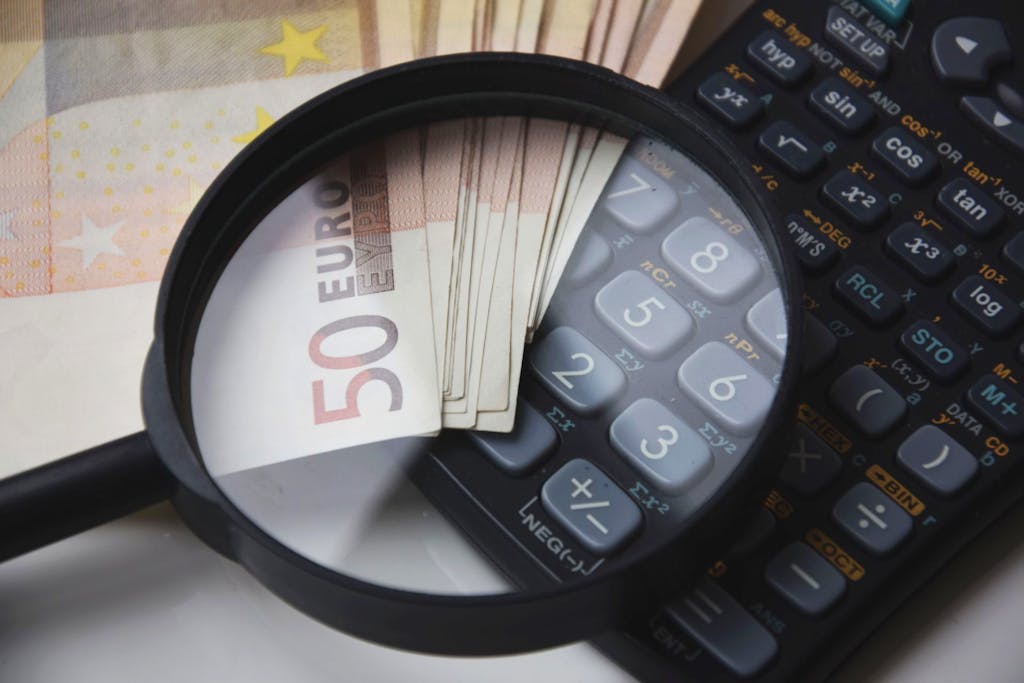 Billets en euros sous une loupe, à côté d’une calculatrice