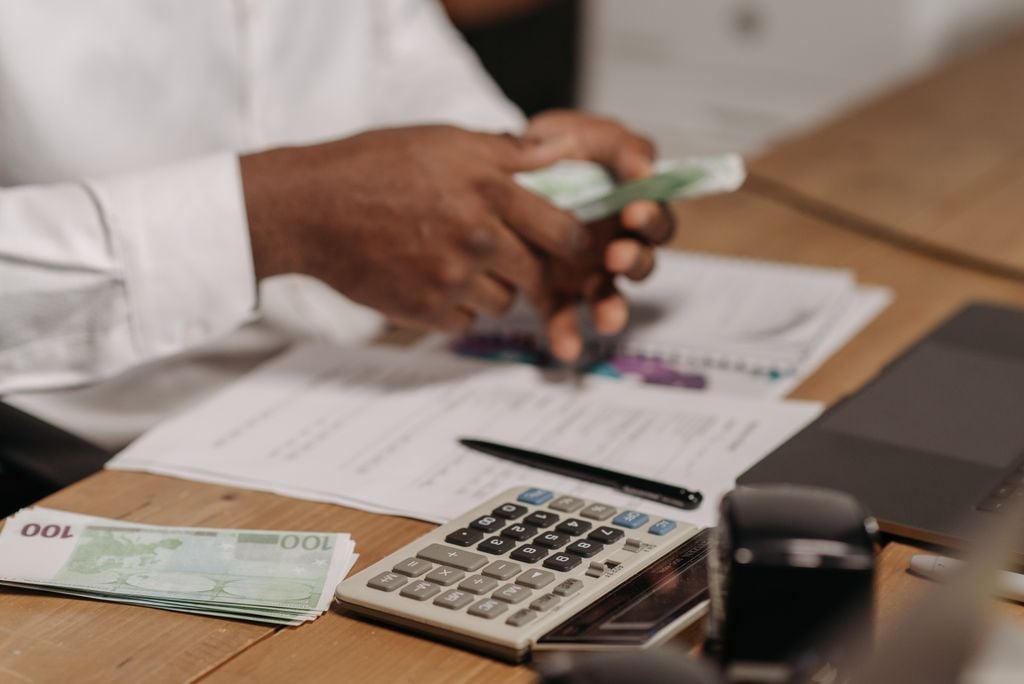 Mains comptant des billets en euros sur un bureau, avec calculatrice et relevés