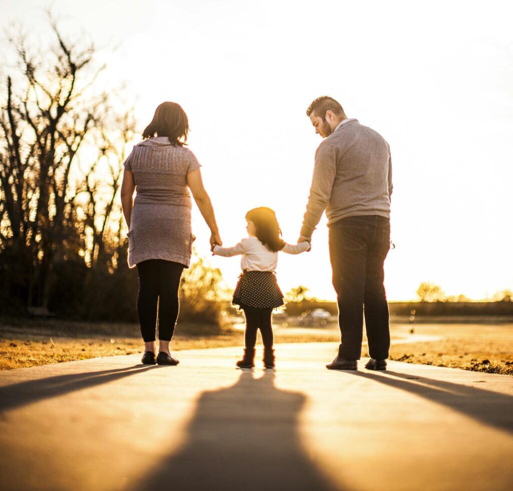 A family of three walks hand in hand at sunset, enjoying togetherness and warmth.