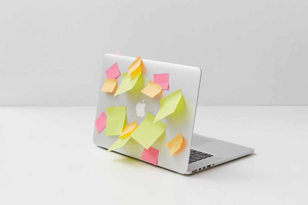 A laptop overloaded with colorful sticky notes on a white desk, symbolizing organization and creativity.