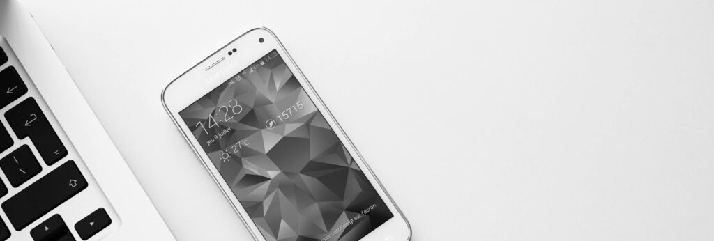 A minimalist office desk with a laptop and smartphone displaying a geometric wallpaper.