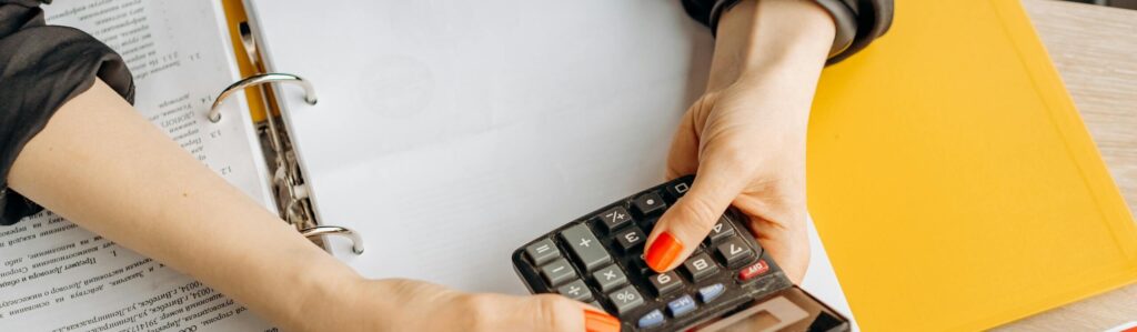 Hands using a calculator at a desk with documents and folders, ideal for finance or accounting themes.